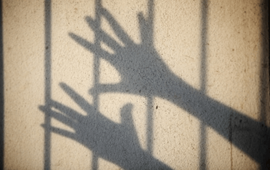 Shadow of hands behind bars