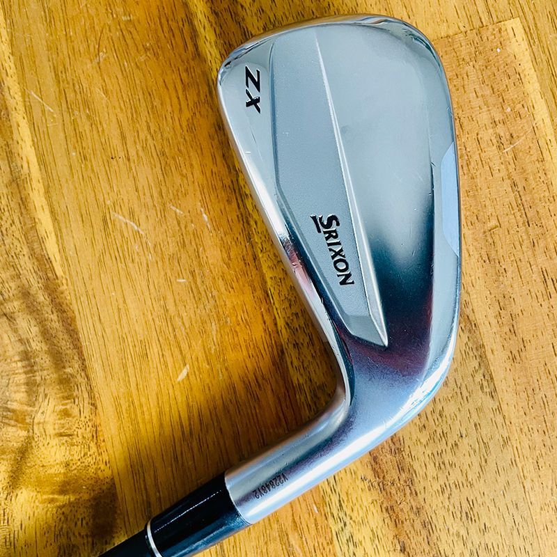 Srixon ZX golf iron on a wooden surface, angled view, silver and black details.