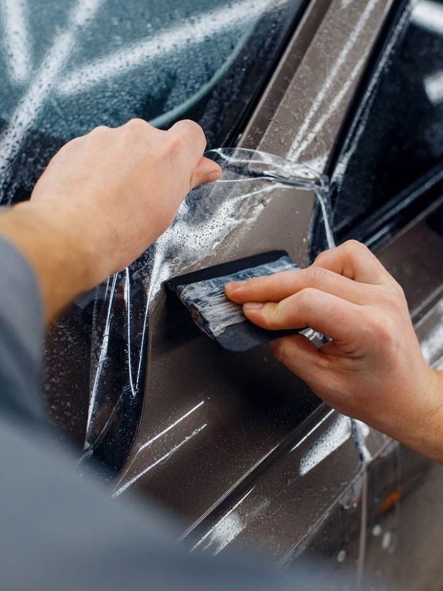 A person is applying a protective film to a car.