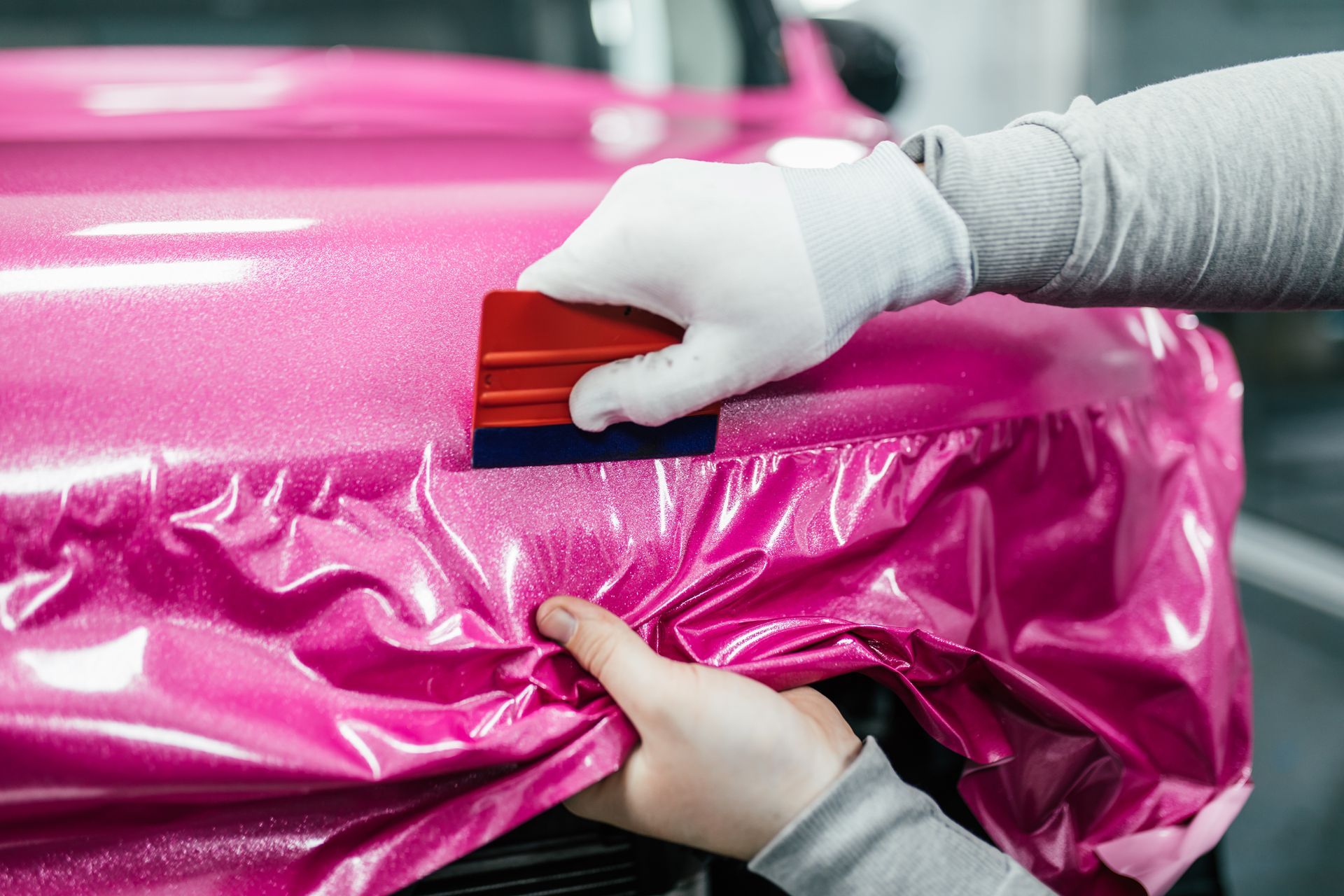 A person is wrapping a pink car with a squeegee.