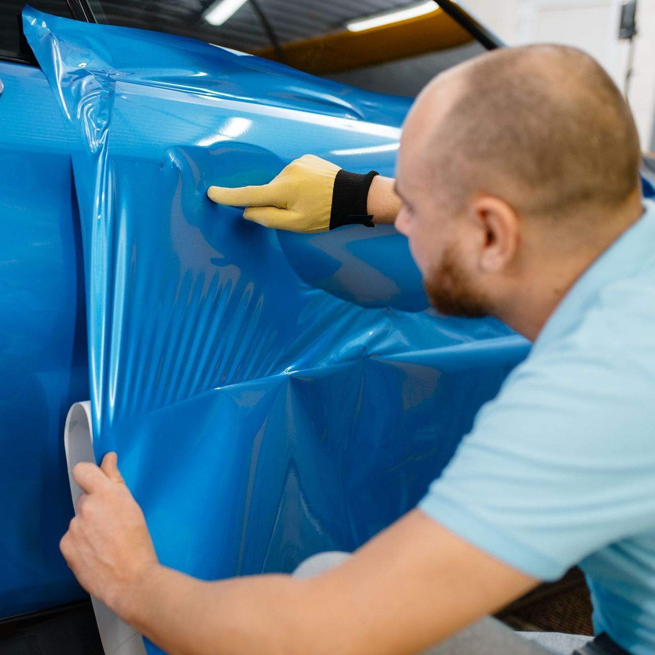 A man is wrapping a blue car with blue plastic