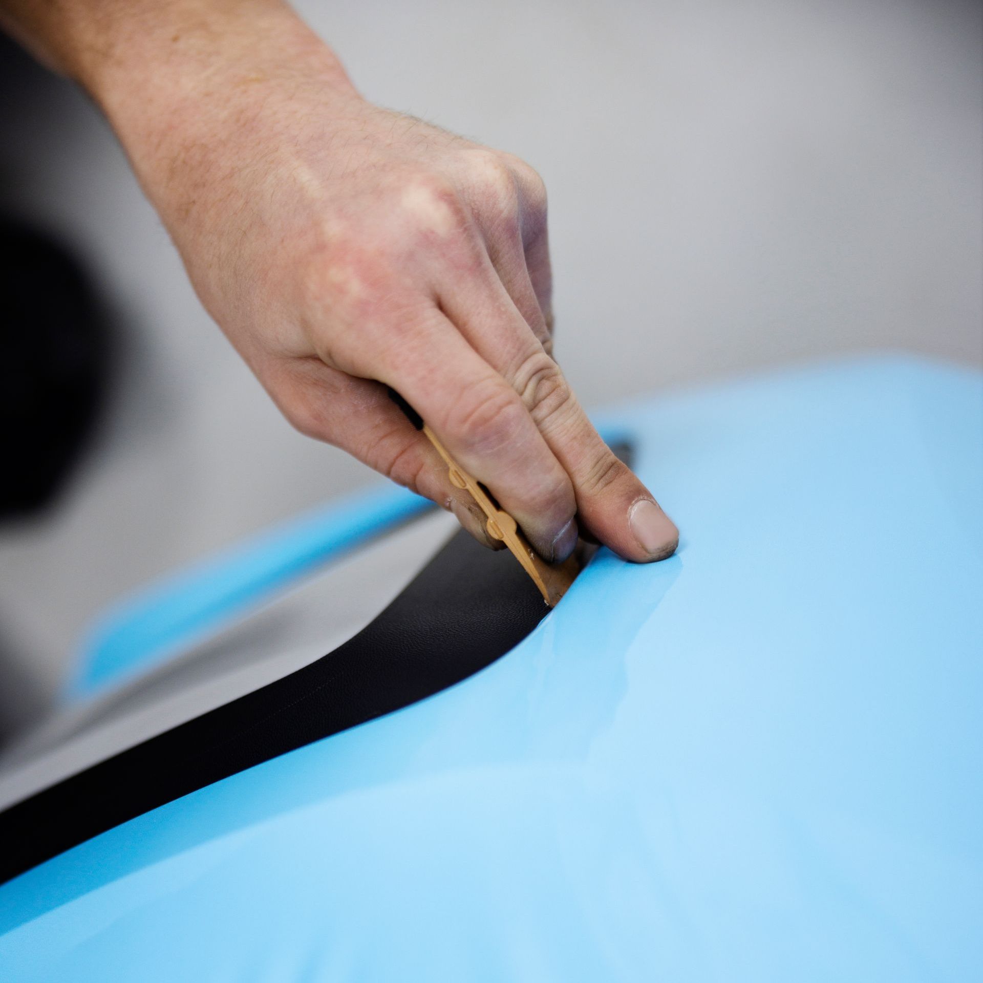 A person is sanding a piece of black tape on a blue surface