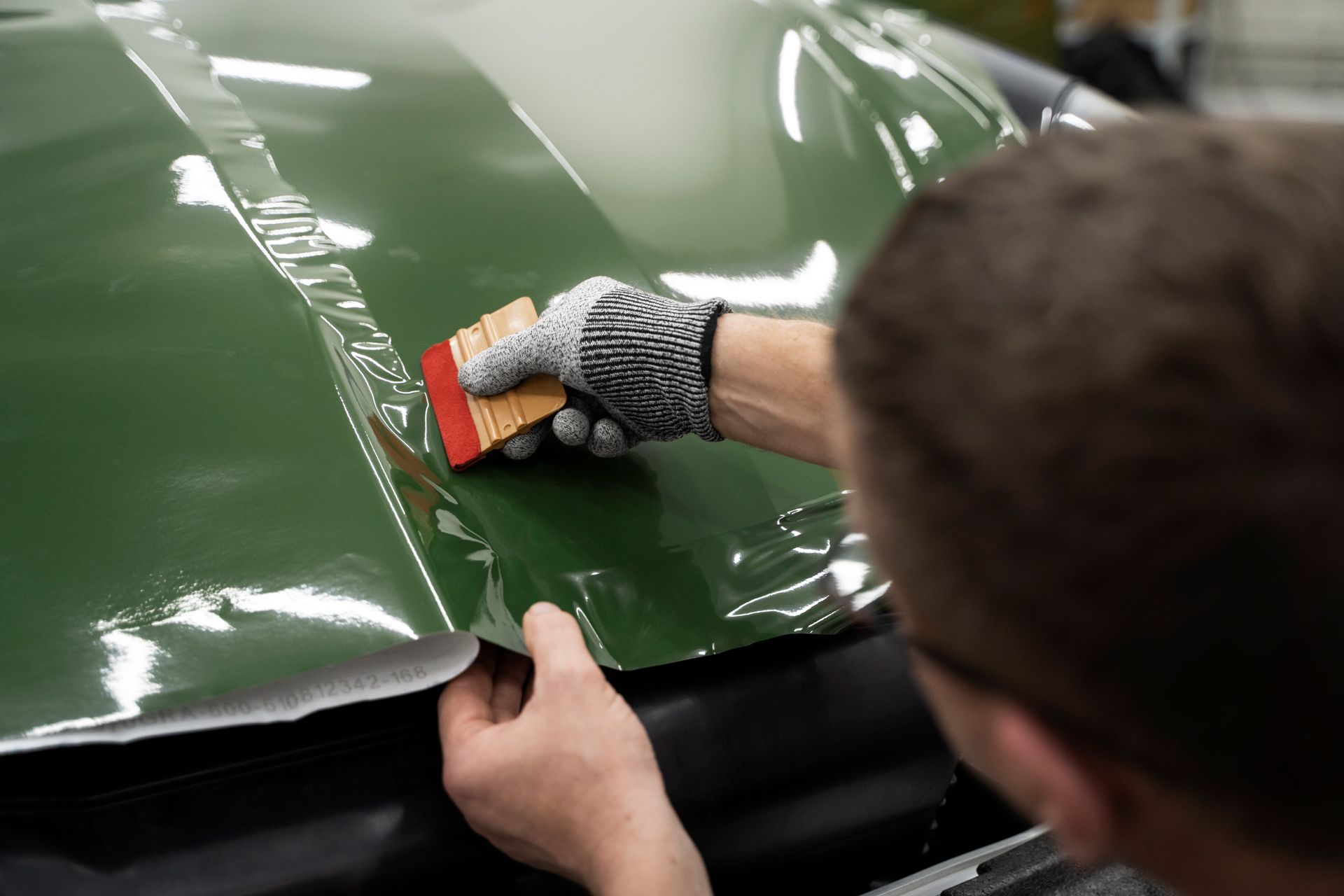 A man is wrapping a green car with a brush.