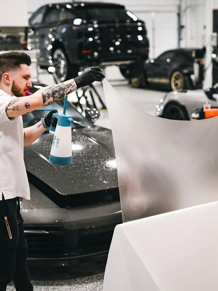 A man is spraying a car with a spray bottle in a garage.