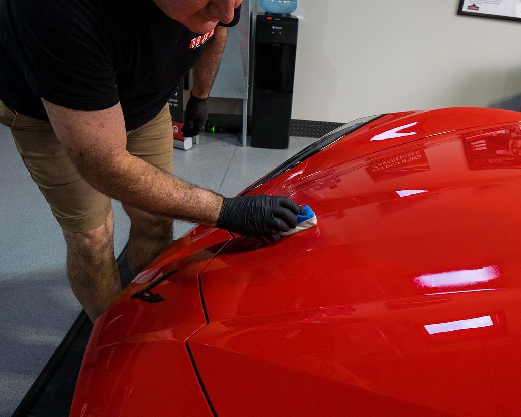 A man is polishing the hood of a red car.