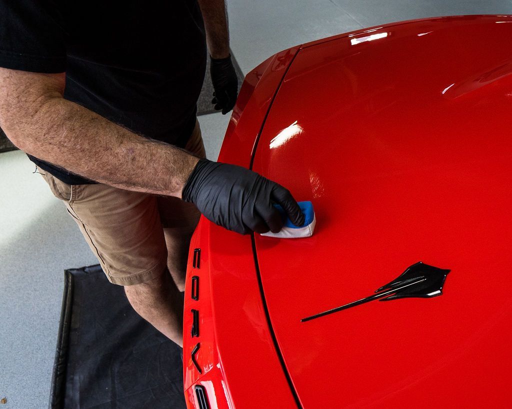 A man is polishing the hood of a red car.