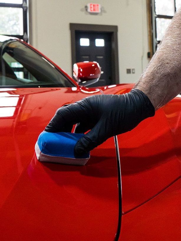 A person wearing black gloves is polishing a red car