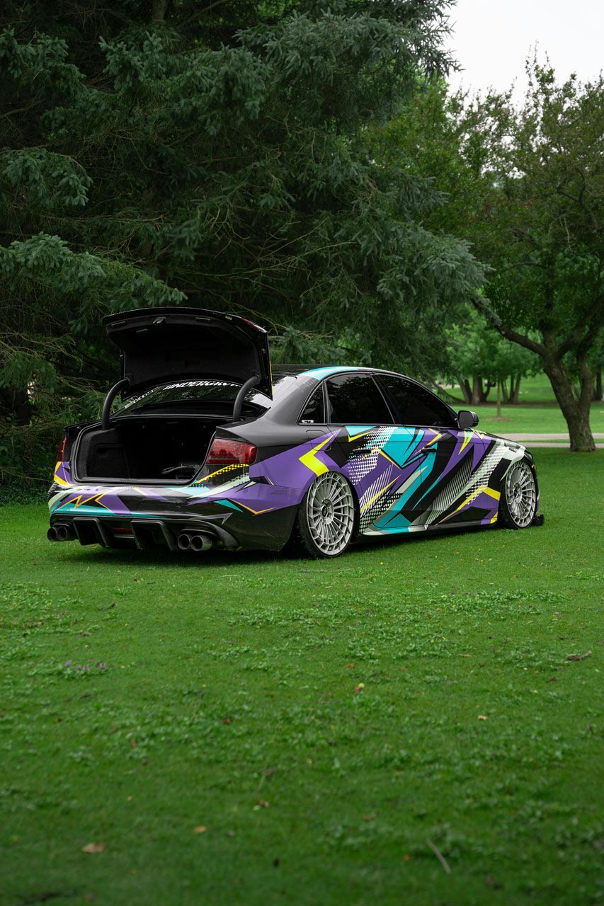 A purple car with the trunk open is parked in a grassy field.