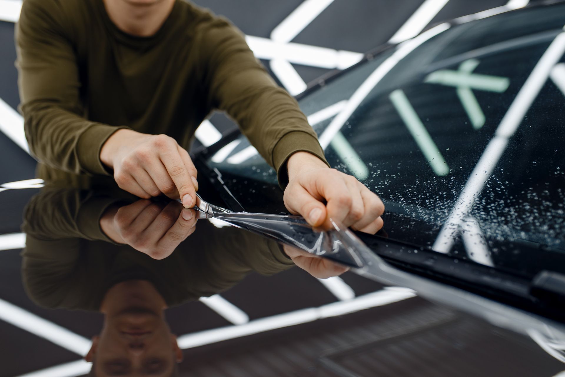 A man is applying a protective film to the hood of a car.