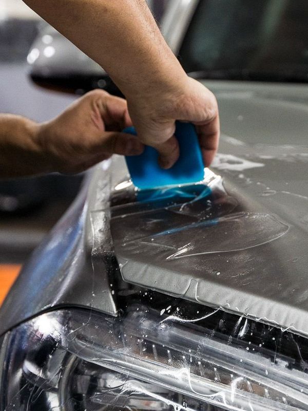 A person is applying a protective film to the hood of a car.