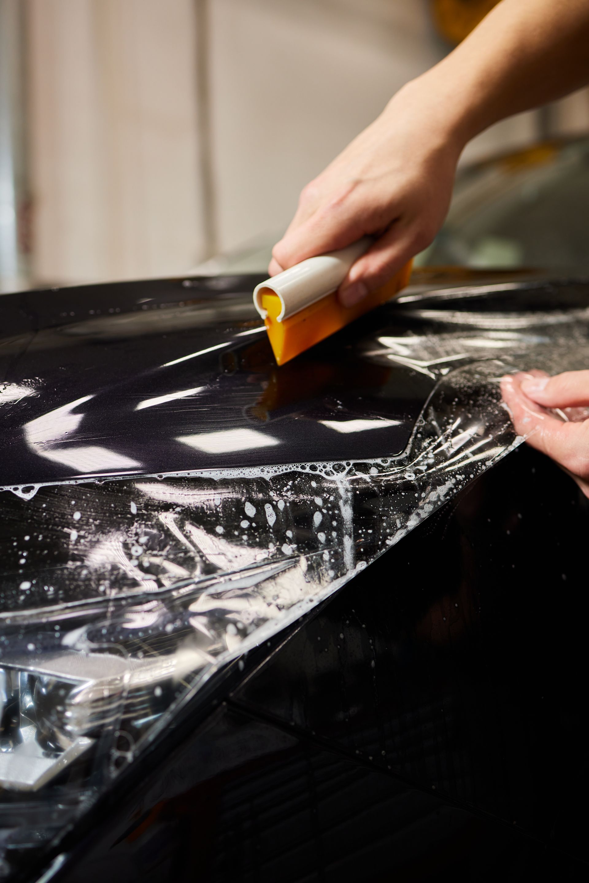 A person is applying a protective film to a car hood.