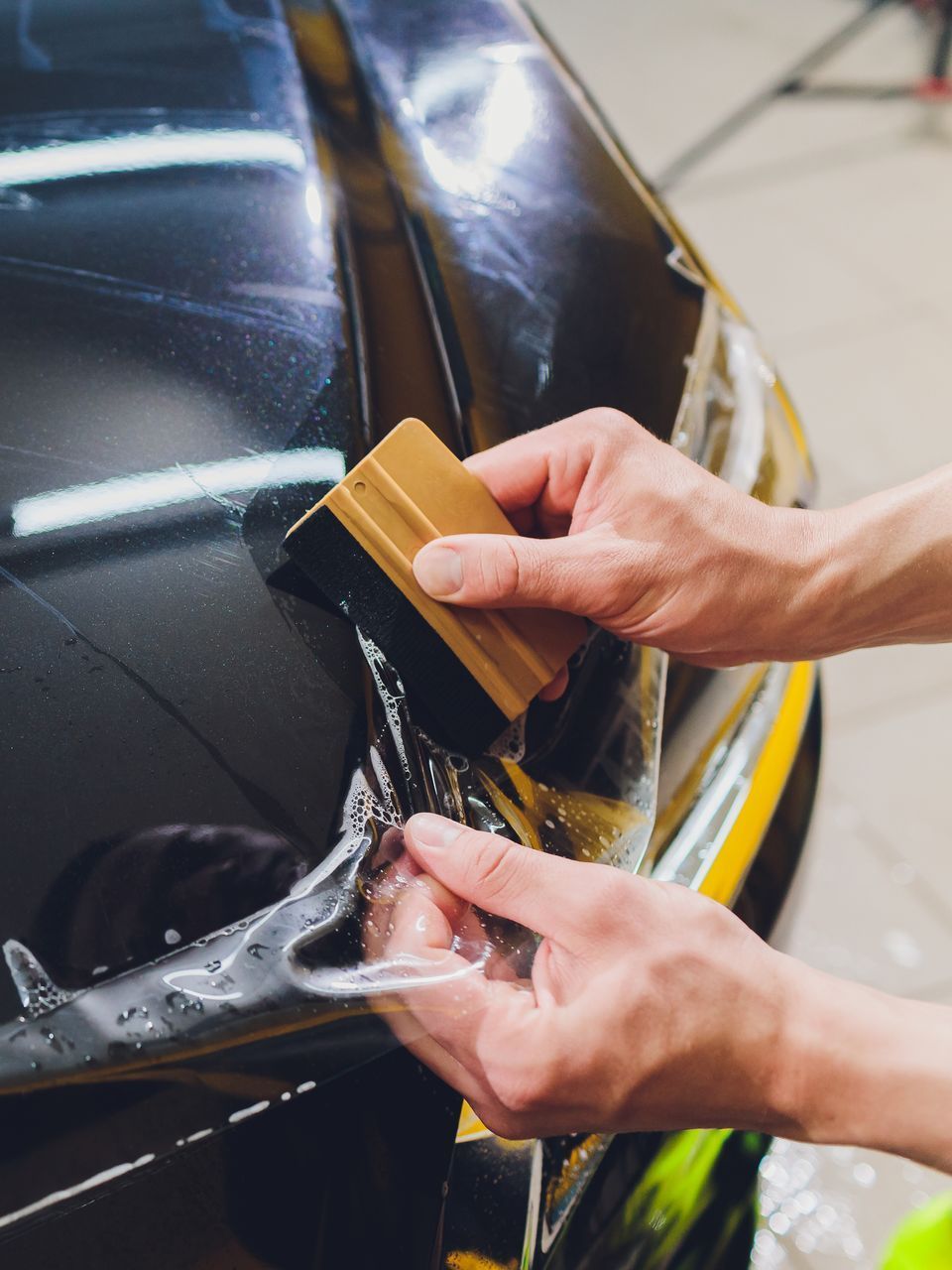 A person is applying a protective film to the hood of a car.