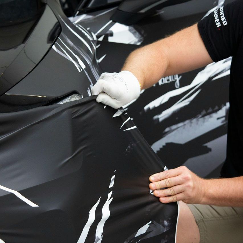 A man is wrapping a car with a black shirt that says motorsport