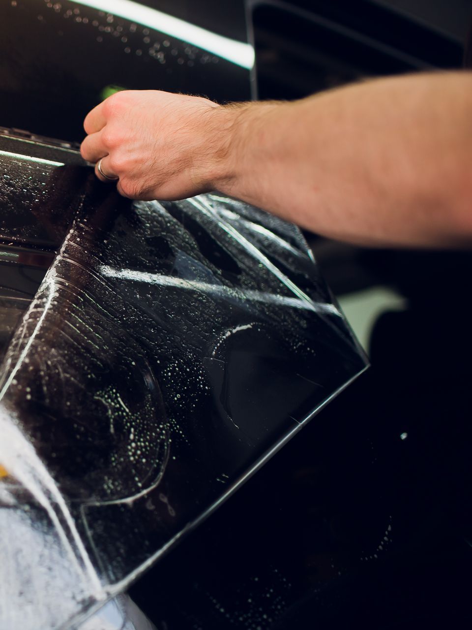 A man is applying a protective film to the side of a car.