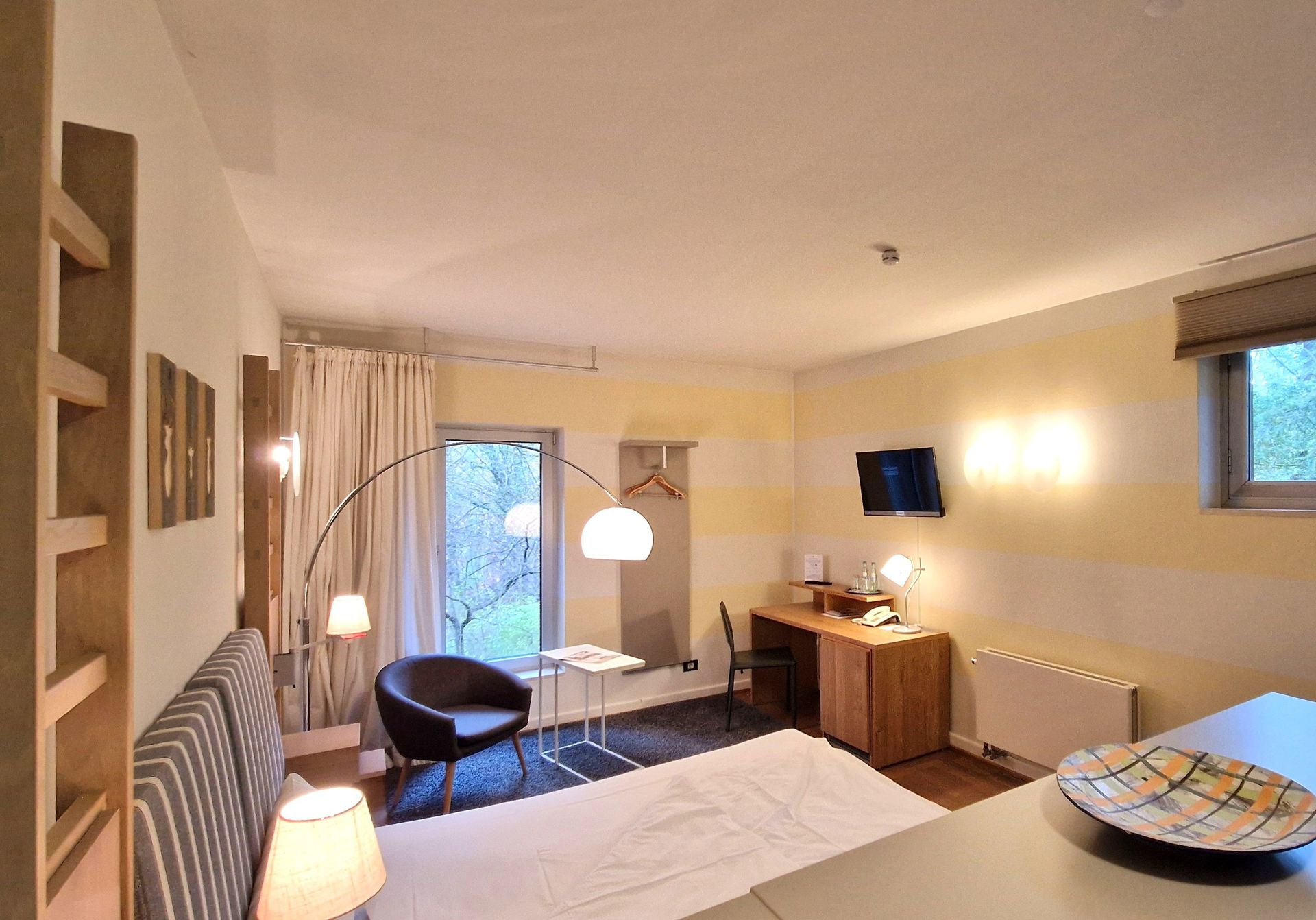 Hotelzimmer mit Bett, Schreibtisch und Balkontüren mit Blick ins Grüne.