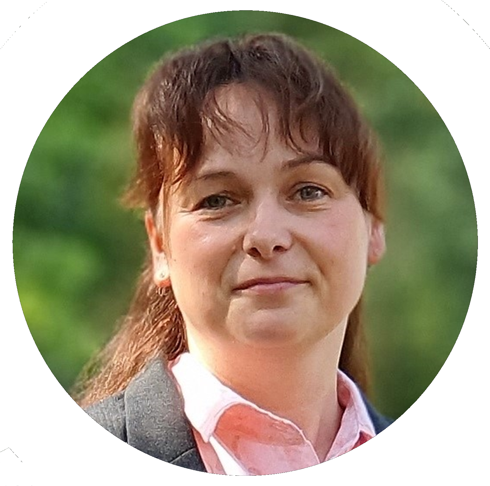 Frau mit braunem Haar und rosa Hemd, die den Betrachter ansieht, im Freien vor grünem Hintergrund.