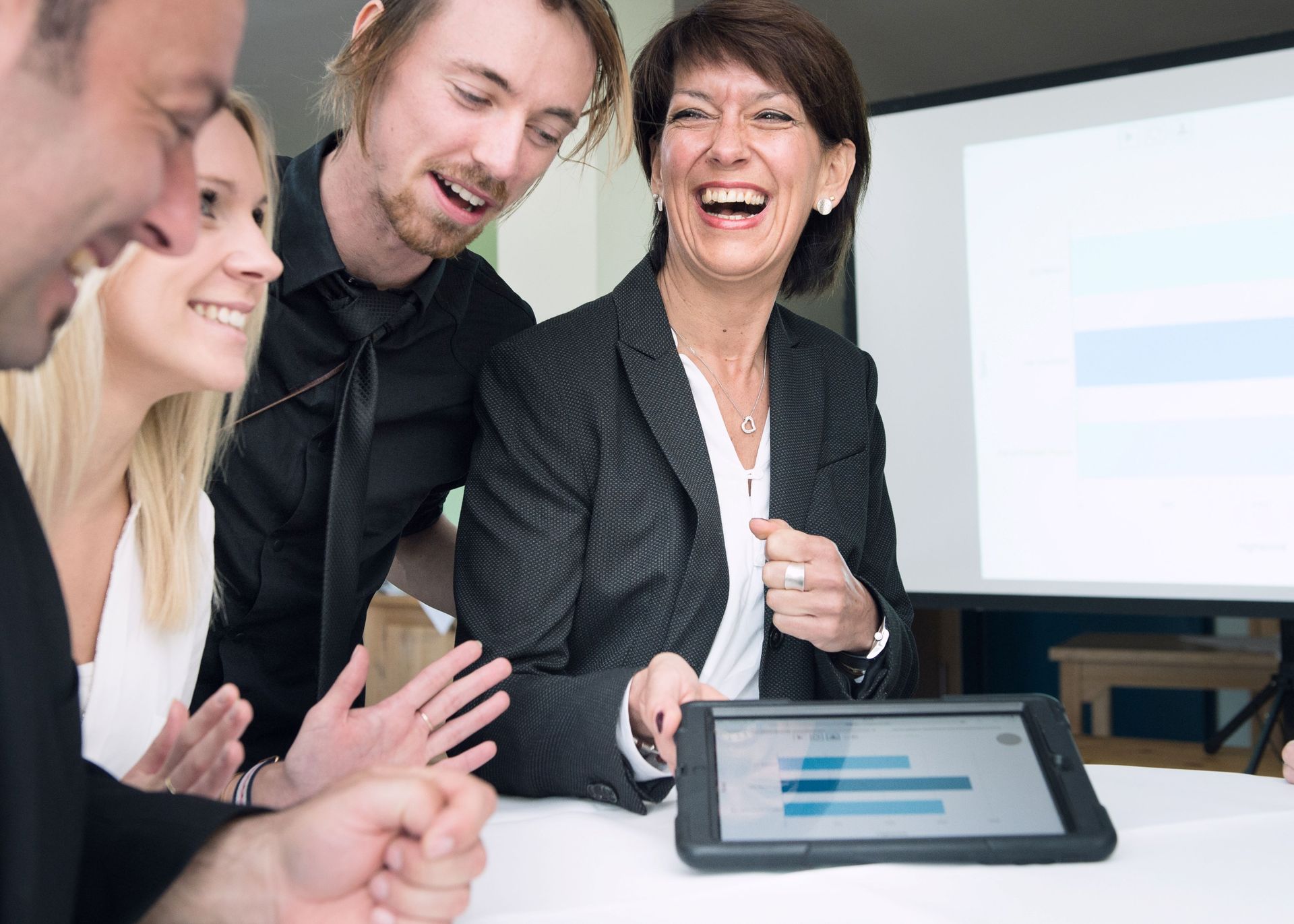 Eine Gruppe von Kollegen lacht, während sie auf ein Tablet mit Datenanzeige schauen.