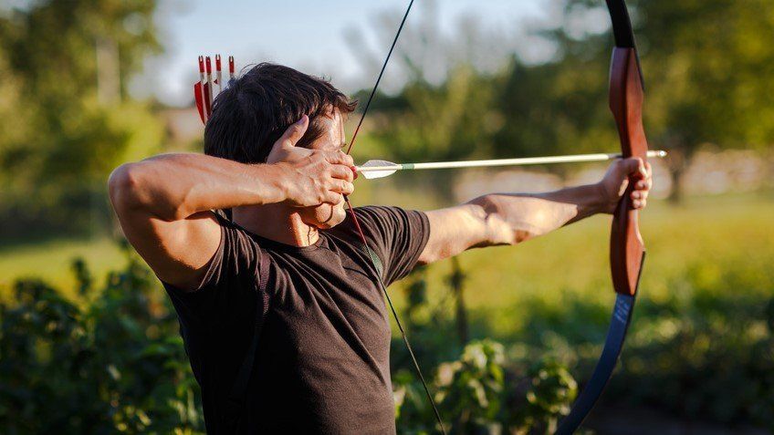 Mann spannt Pfeil und Bogen und zielt im Freien auf ein Ziel.