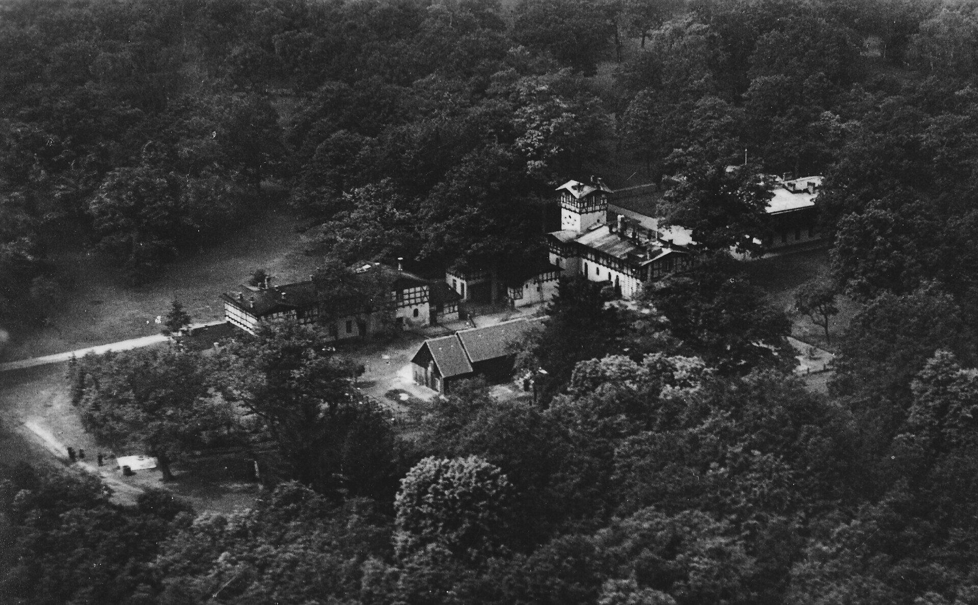 Luftaufnahme eines von dichten Bäumen umgebenen Gebäudekomplexes, wahrscheinlich ein abgelegenes Anwesen.