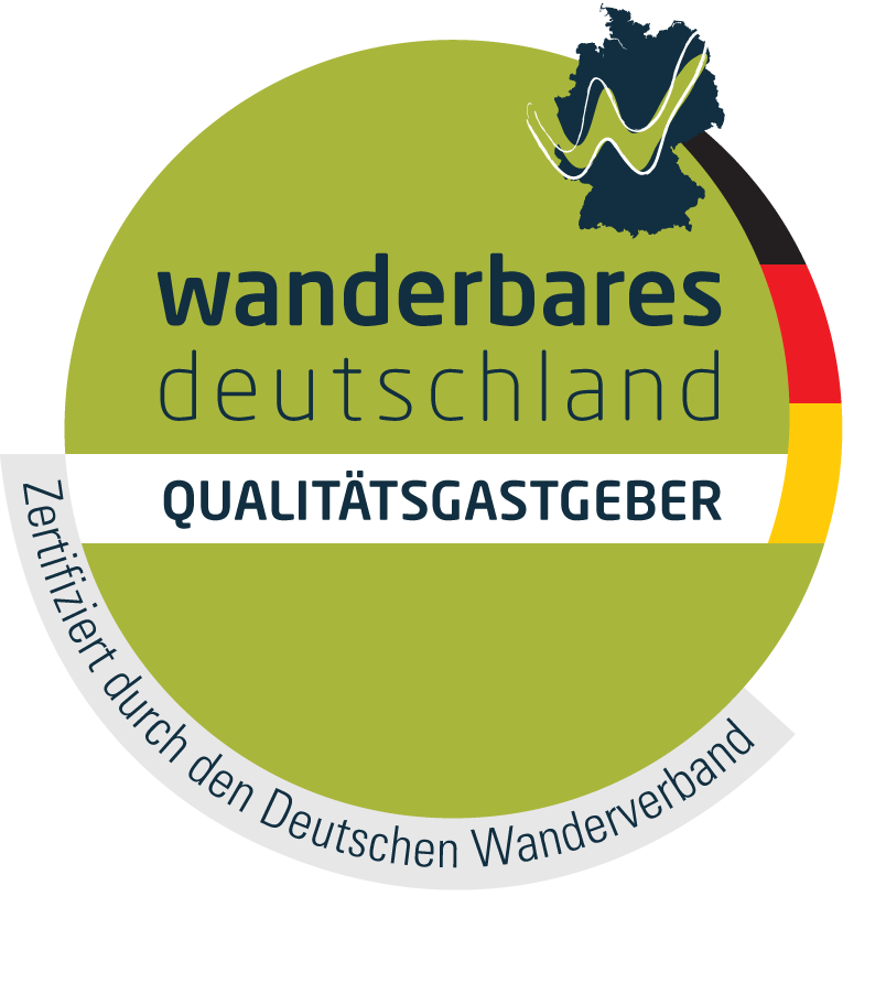Grünes, rundes Logo: „Wanderbares Deutschland“ mit Deutschlandkarte, den Farben der deutschen Flagge und dem Text „Qualitätsgastgeber“.