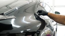 Gloved hand applying a coating to a shiny black car. Garage setting with bright reflections.