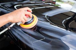 A person using a rotary buffer to polish a black car hood, creating swirls.