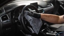 Person wearing black gloves cleaning car steering wheel with gray cloth.