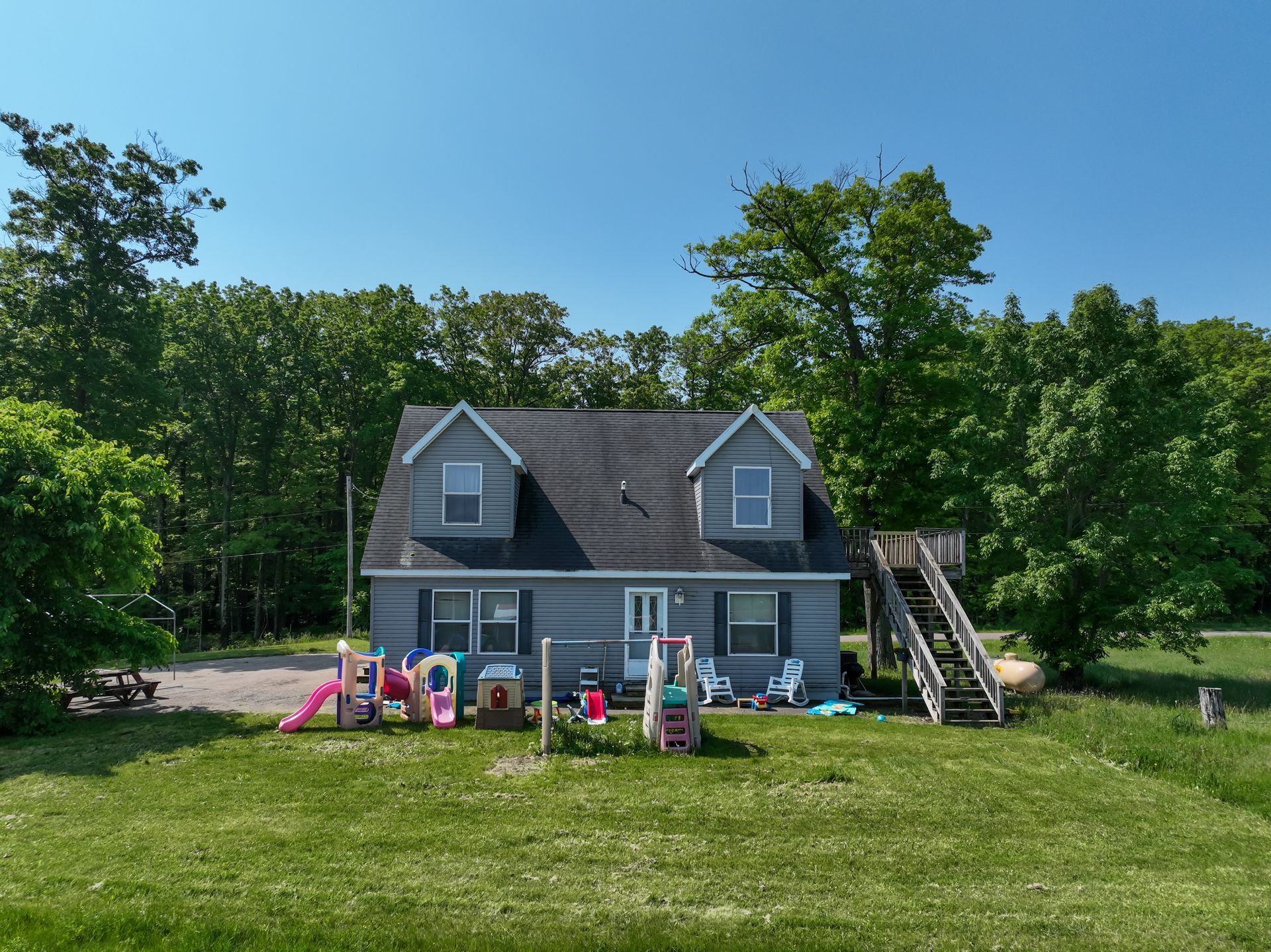 Gray house with a playground in the yard, backed by trees, under a blue sky.