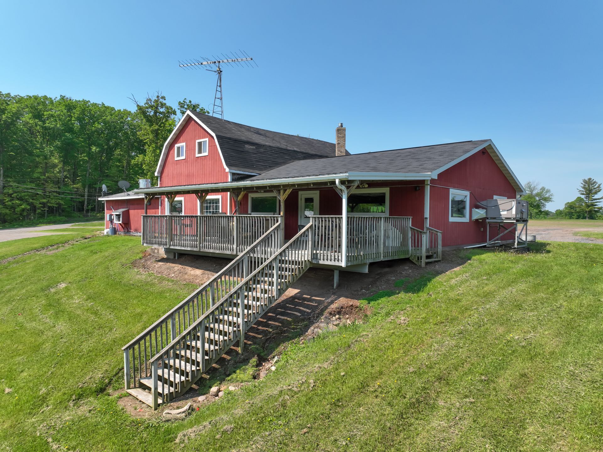 Red building with a deck and stairs on a grassy hill; a blue sky in the background.