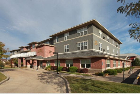 Multi-story brick and gray building with a curved driveway and blue sky.