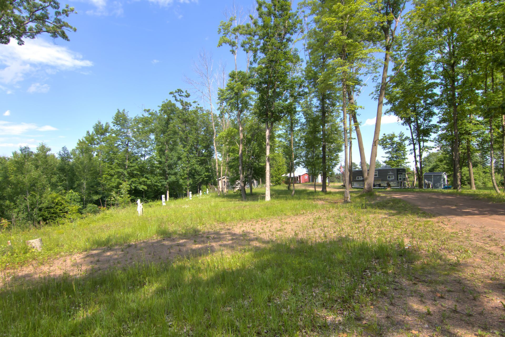 Grassy field with sparse trees, fence posts, and buildings in the distance against a blue sky.