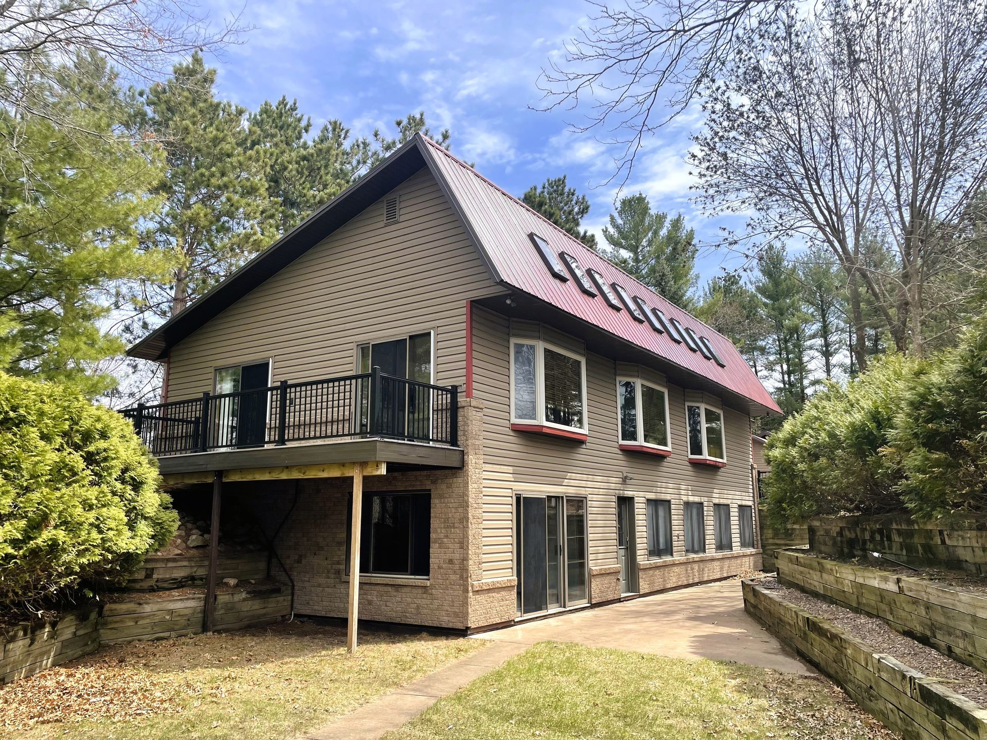 Two-story house with brick and siding, balcony, red roof, surrounded by trees and grass.