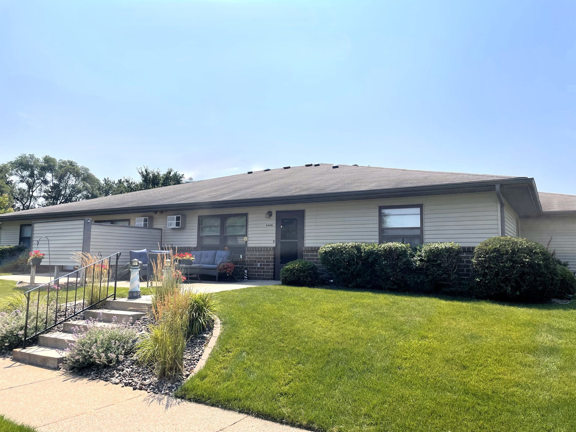 Single-story beige apartment building with green lawn, sidewalk, and blue sky.
