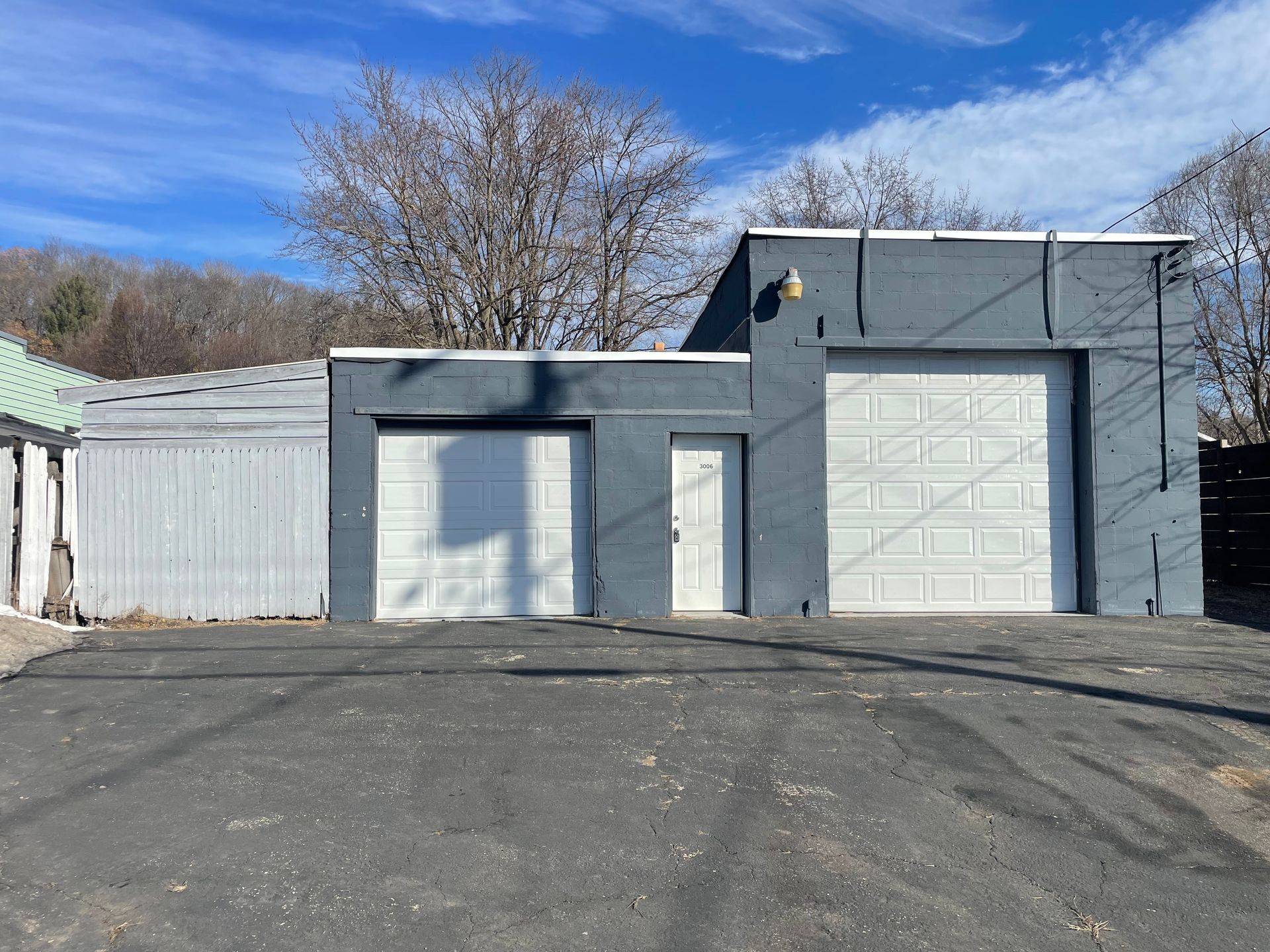 Two gray garage doors and a white door on a gray building under a blue sky.