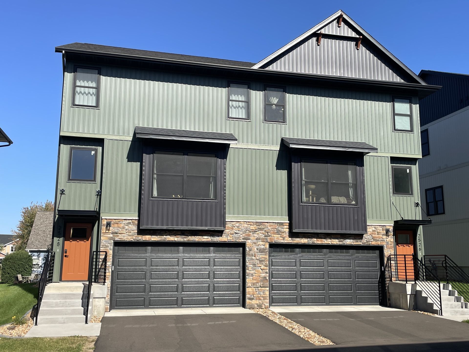 Two-story townhouses with green siding, black garage doors, and stone accents.