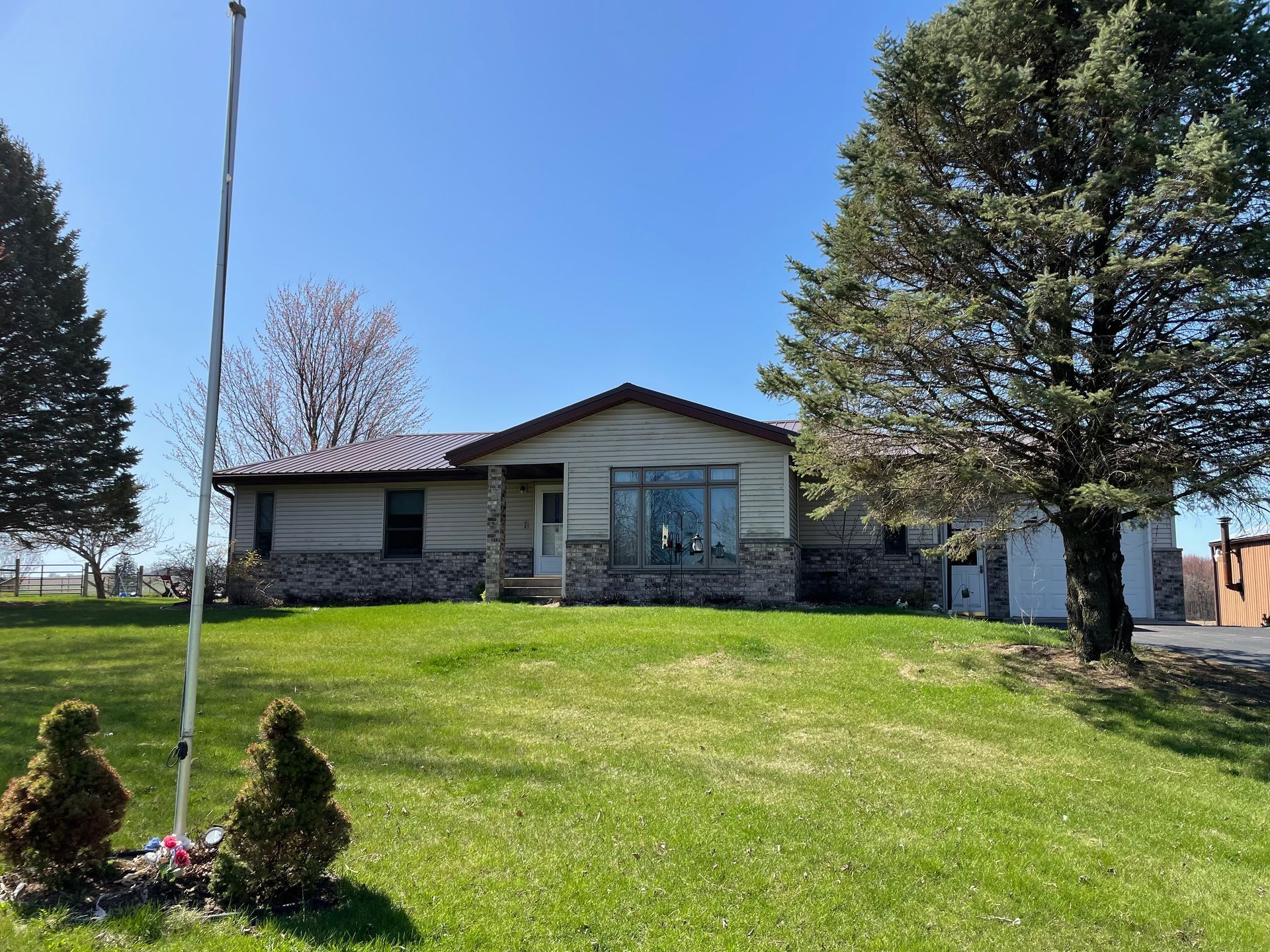 Ranch-style house with stone and tan siding, green lawn, trees, and a blue sky.