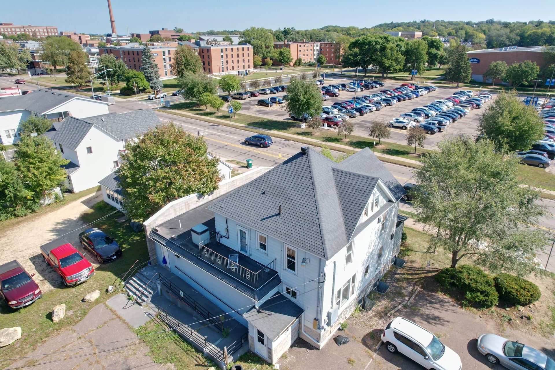Aerial view of a white multi-story building, cars parked in front and a large parking lot.