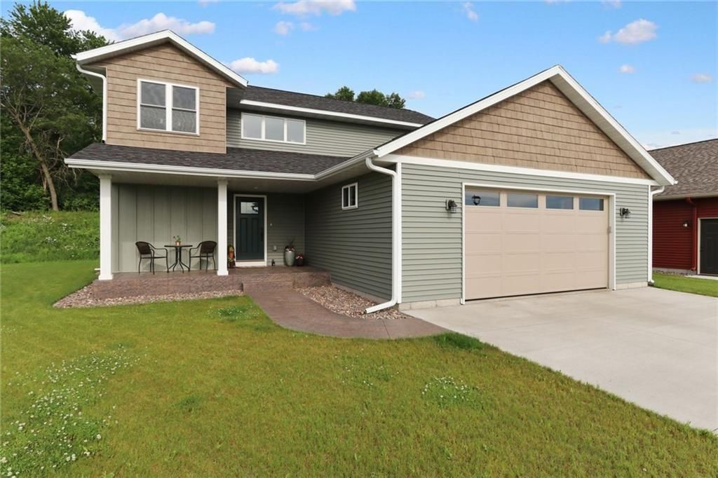 Green two-story house with tan accents, a garage, and a small front yard on a sunny day.