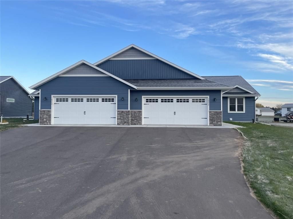 Blue duplex with white garage doors and stone accents, on a paved driveway under a blue sky.