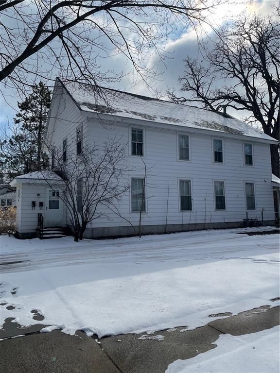 White two-story house in winter, covered in snow. Bare trees and overcast sky.