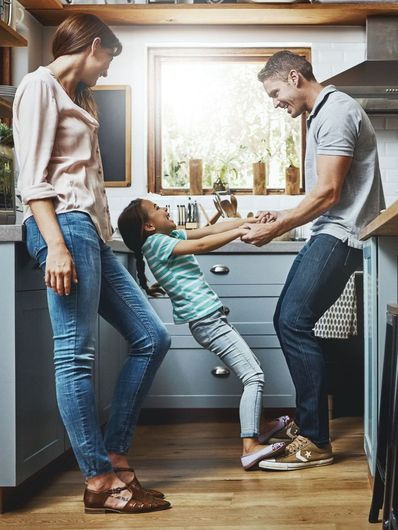 A family is playing with a little girl in a kitchen.