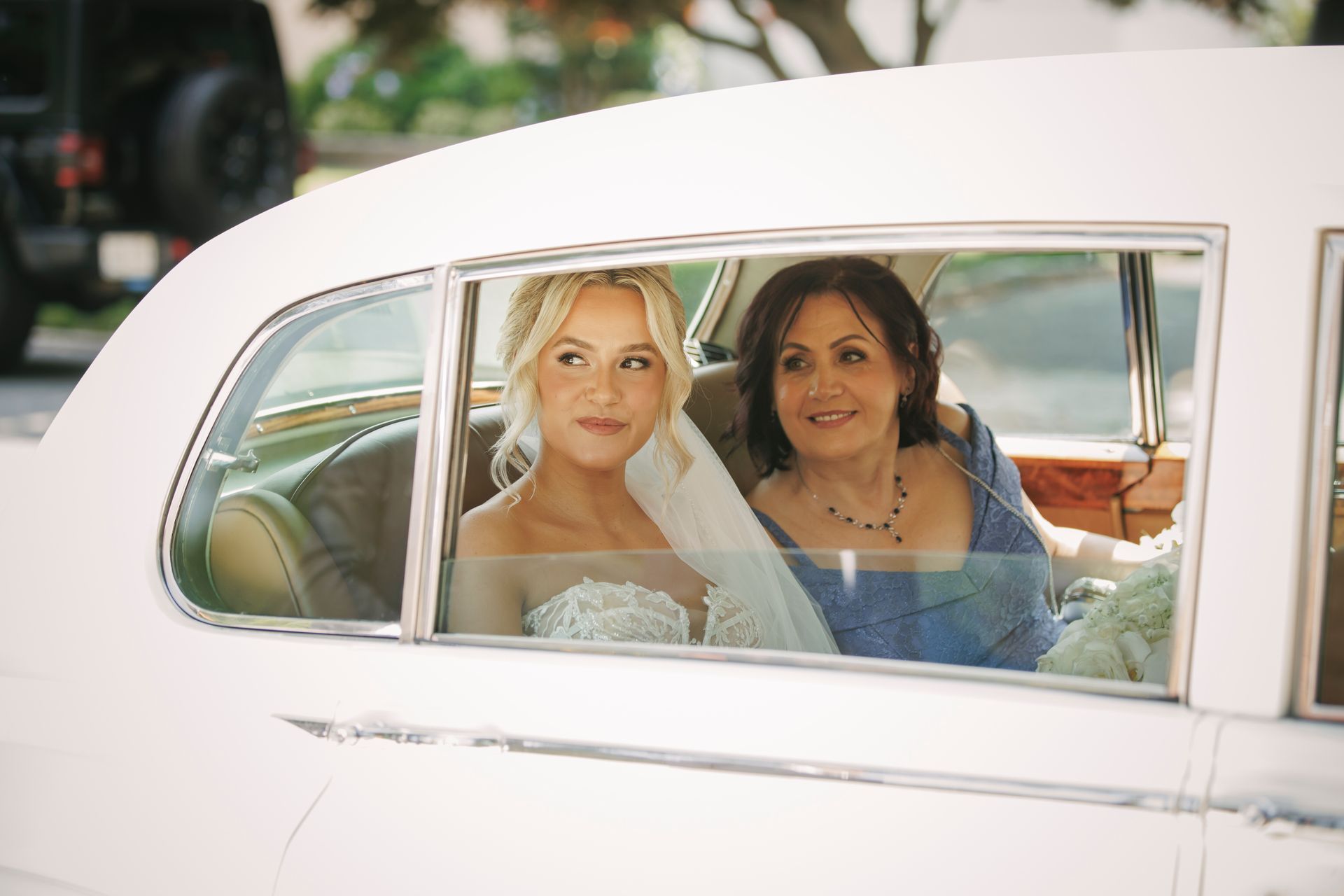 A bride and her mother are sitting in a white car.