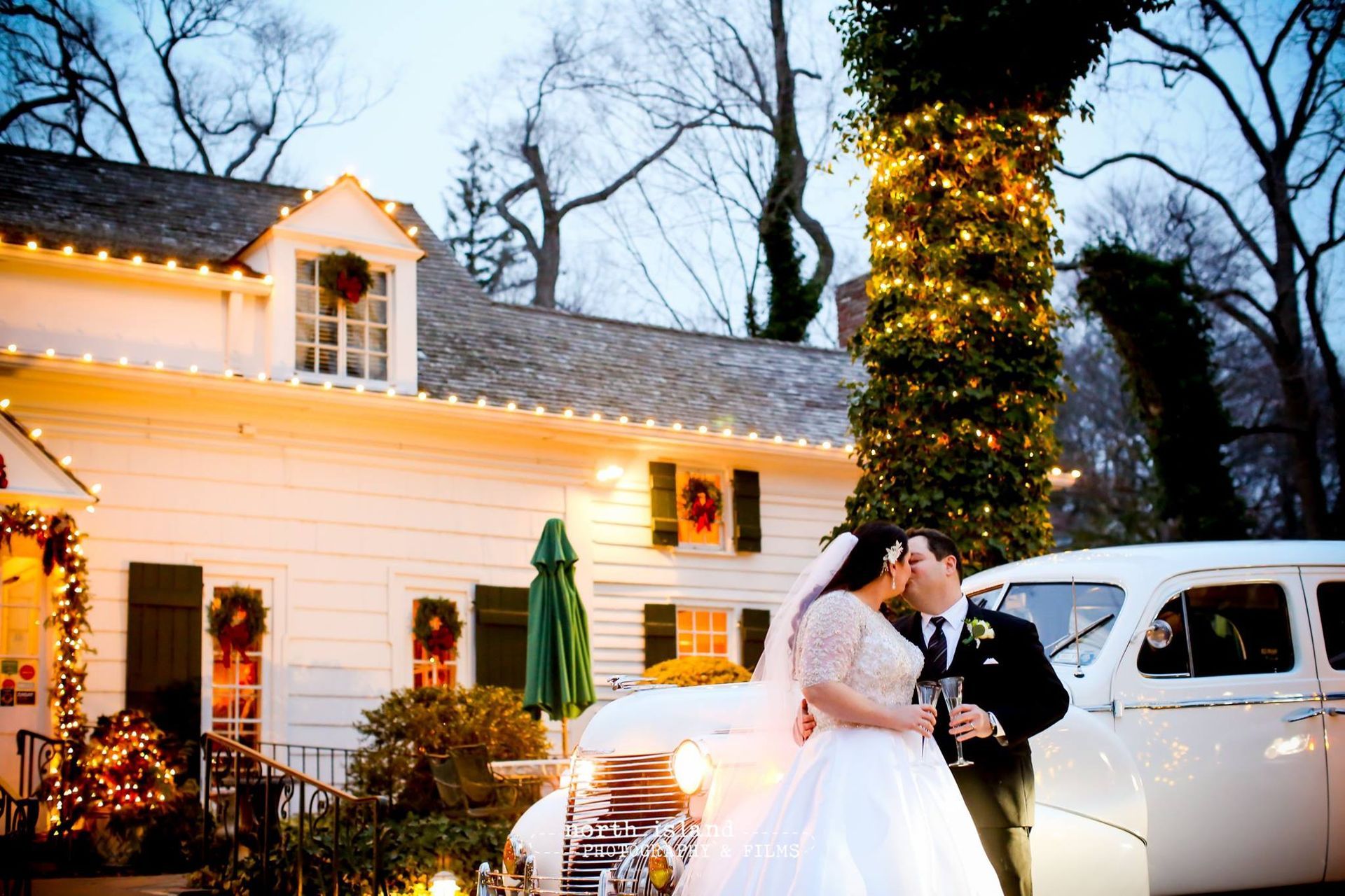 A bride and groom are posing for a picture in front of a white car.