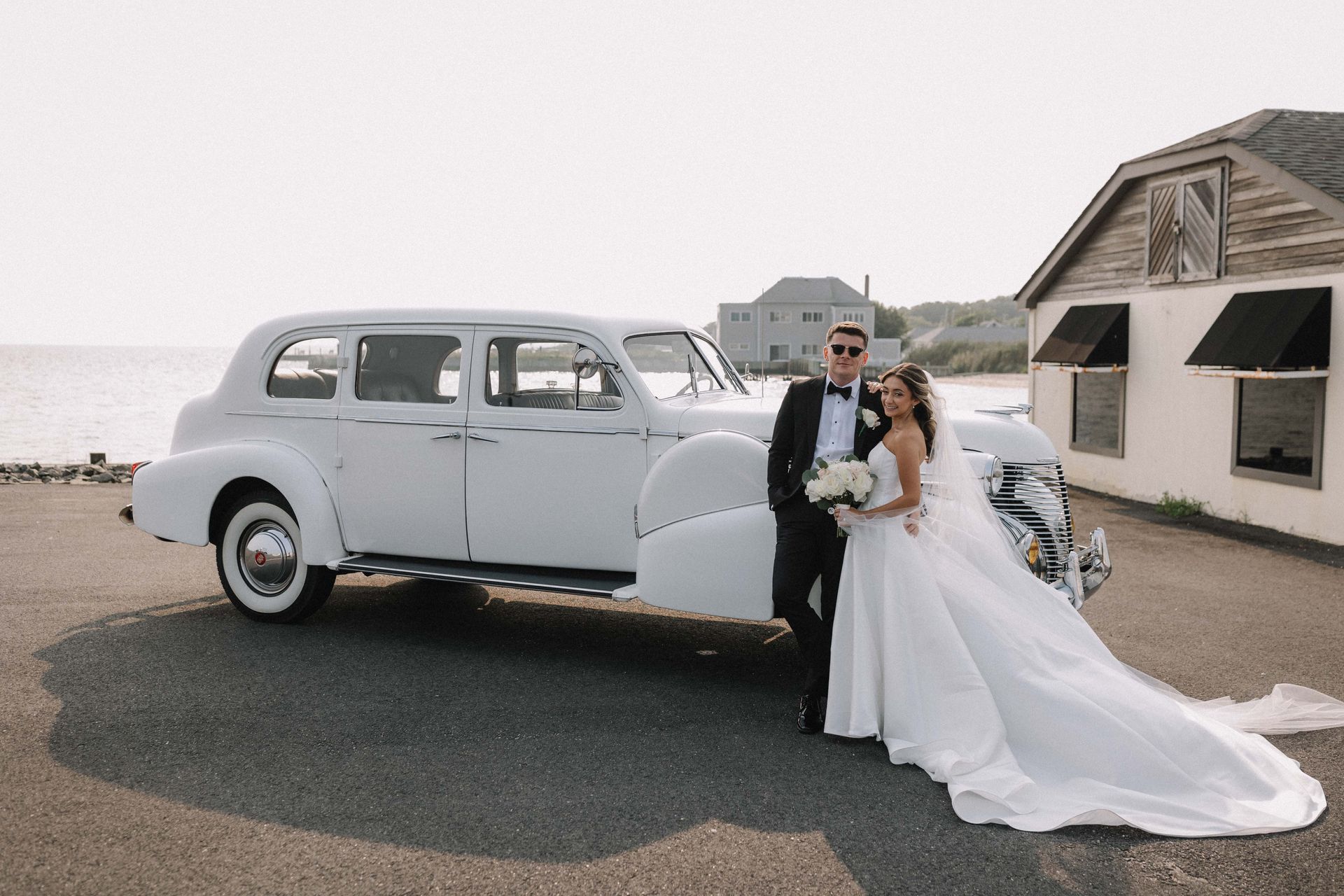 A bride and groom are posing for a picture in front of a white limousine.