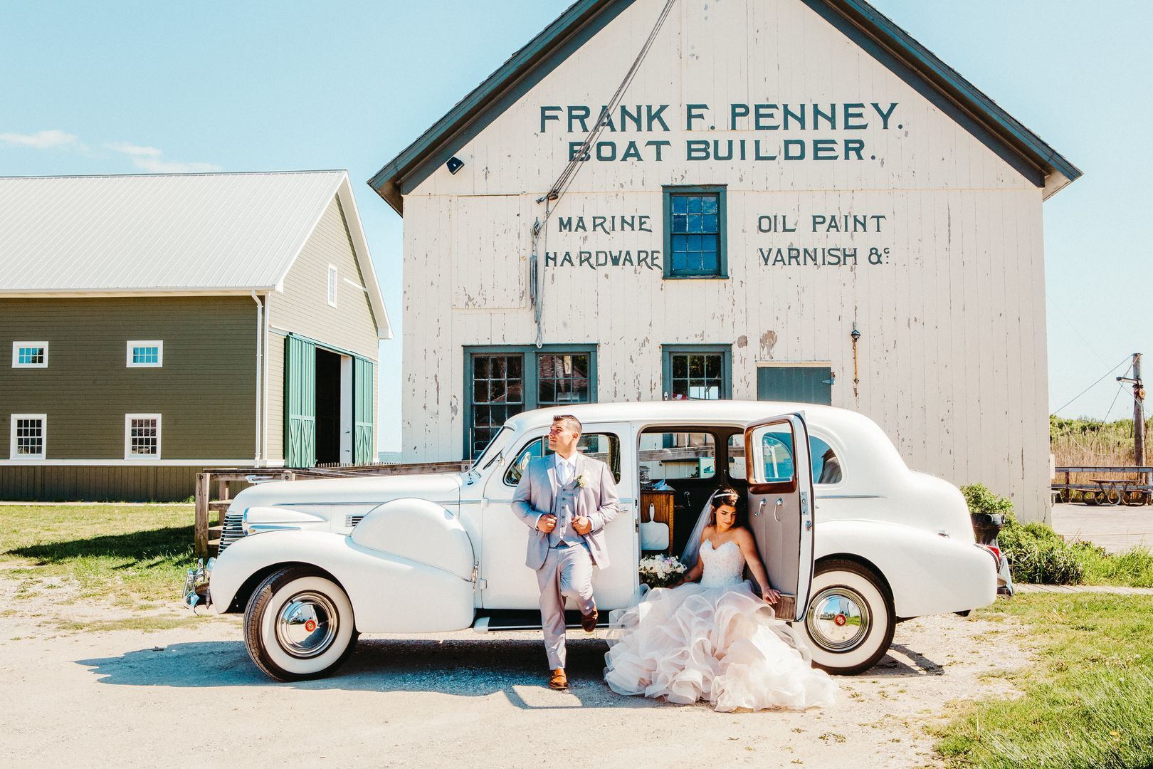 A bride and groom are posing for a picture in front of a white car.