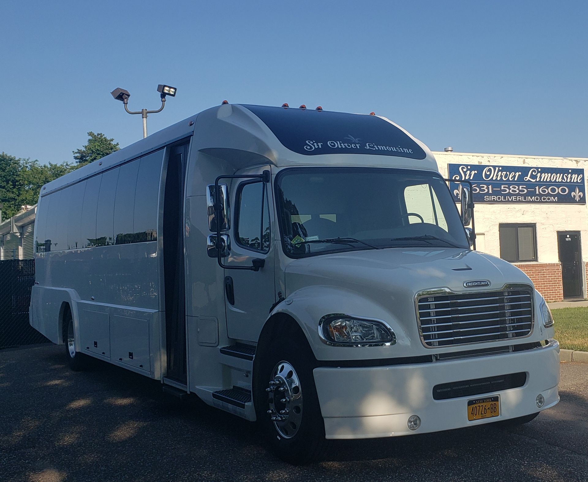 A white bus is parked in front of a building that says mr. oliver limousine