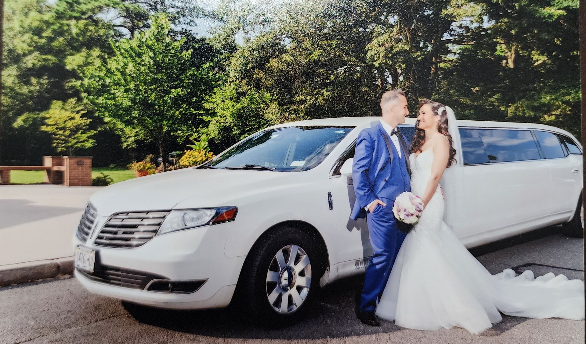 A bride and groom are standing next to a white limousine.