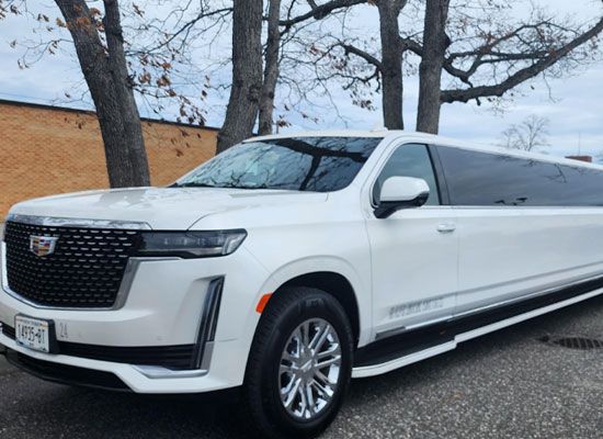 A white cadillac escalade limousine is parked in front of a building.