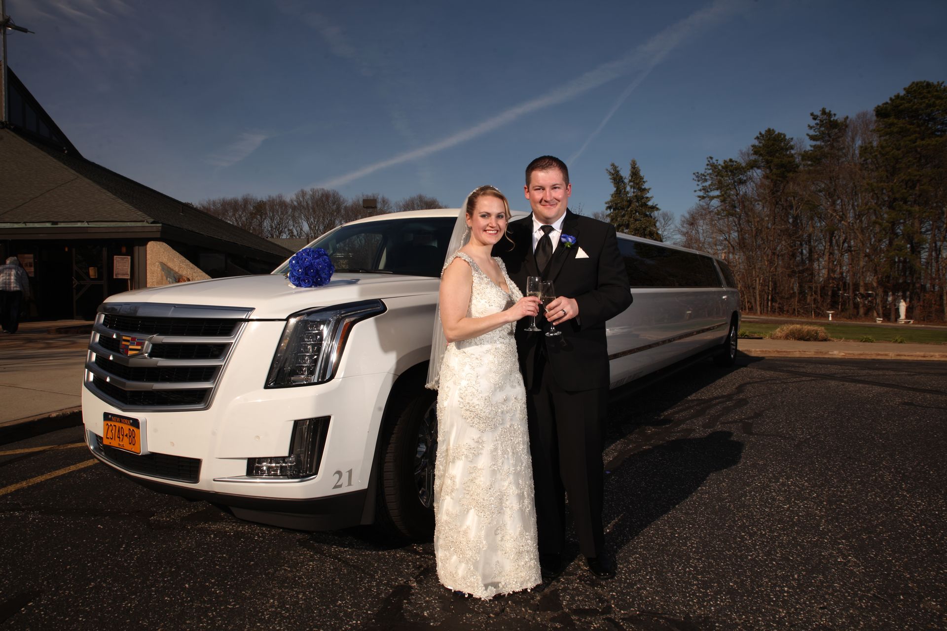 A bride and groom are posing for a picture in front of a white limousine.