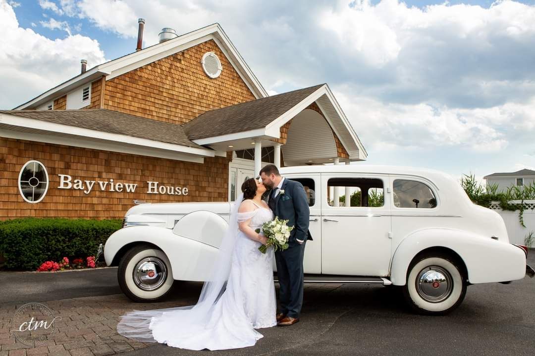 A bride and groom are kissing in front of a white car.